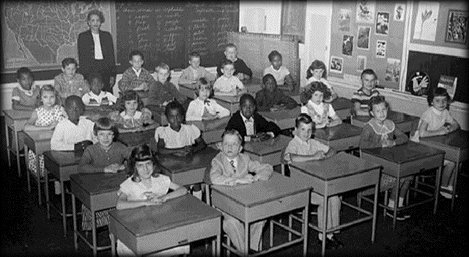 A 19th-century classroom with separated desks, each with personal storage, facing away from the blackboard